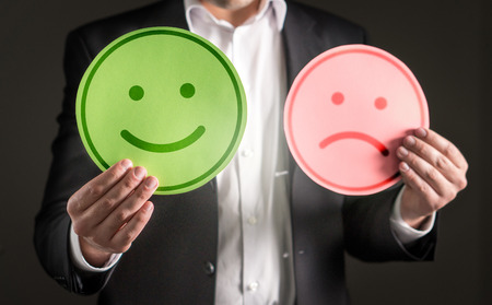 Business man with happy smiling and sad unhappy cardboard paper smiley face emoticon. Rating and giving review about customer satisfaction or team spirit in company.の写真素材