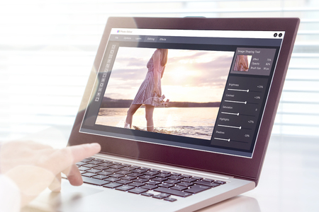Photo editing. Professional editor retouching an image with laptop and imaginary computer software. All graphics are made up.の写真素材