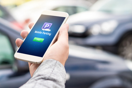 Mobile parking app on smartphone screen. Man holding smart phone with car park application in hand. Internet payment online with modern device.の写真素材