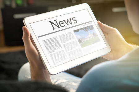 Man reading the news on tablet at home. Imaginary online and mobile news website, application or portal on modern touch screen display. Holding smart device in hand.の写真素材