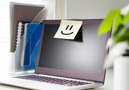 Good working environment and happy atmosphere in workplace. Team spirit. Smiley face drawn on a sticky paper and post it note on laptop in office workstation.の写真素材