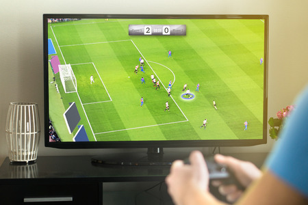 Young man hanging out and playing imaginary soccer or football video game with console and tv. Holding controller in hand. Fun freetime activity.の写真素材