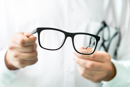 Optician holding glasses. Eye doctor showing new lenses. Professional optometrist in white coat.の写真素材