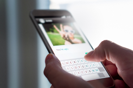 Cyber bullying, internet trolling and bad behavior online concept. Person writing mean comment to picture on an imaginary social media website with smart phone.の写真素材