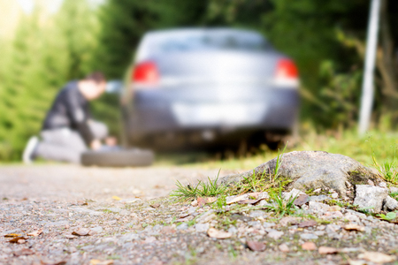 Man changing new spare wheel after vehicle hit rock on countryside sand road. Broken and flat car tyre in forest. Driver fixing problem.の写真素材