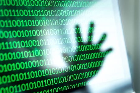 Cyber security threat and attack concept. Binary numbers, zero and one on laptop screen. Reflection of hacker hand in computer monitor.の写真素材