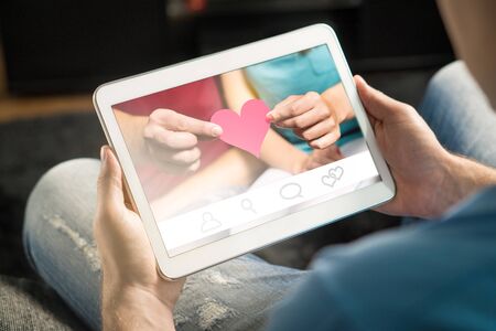 Online dating concept. Imaginary application or website. Finding love from internet using app. Man using and holding tablet and smart device at home.の写真素材