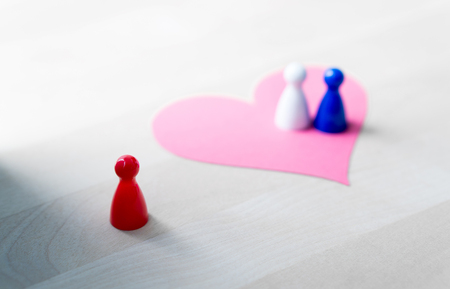 Having affair, infidelity or cheating concept. Love triangle or being third wheel. Board game pawns and paper heart on table.の写真素材