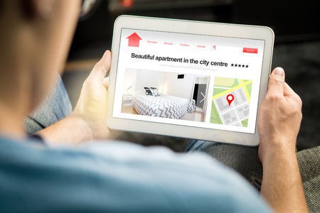 Man search apartments and houses online with mobile device. Holiday home rental or real estate website or application. Imaginary internet marketplace for vacation lodging or finding new home.の写真素材