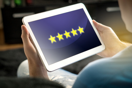 Five star rating and review from satisfied and happy customer and reviewer. Man holding tablet with an imaginary criticism application, social media or website on screen.の写真素材