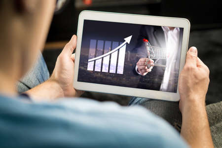 Statistics, analytics and financial report on tablet screen. Success and growth concept. Entrepreneur using business application and doing market analysis with smart mobile device at home.の写真素材