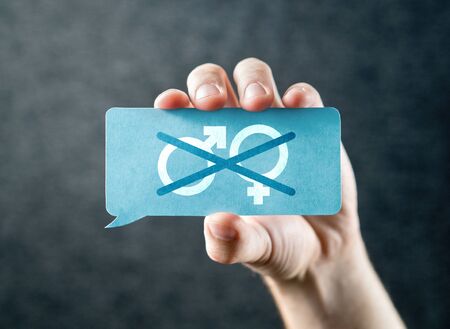 Gender neutrality concept. Crossed out woman and man, female and male symbols. Hand holding a cardboard paper card speech balloon.の写真素材