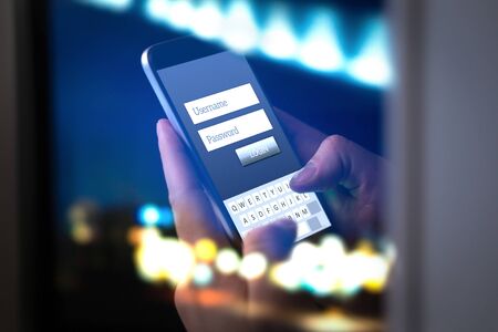 Login with smartphone to online bank account or personal information on internet at night. Hands typing and entering username and password to an application in dark. Cyber security, phisning concept.の写真素材