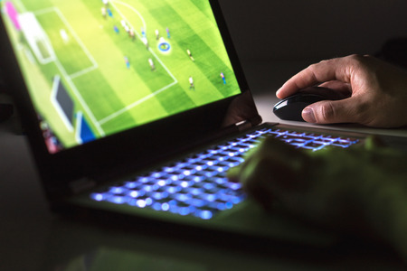Young man playing soccer or football game online with laptop in dark or late at night. Competitive video gaming, electronic sports and esports concept.の写真素材