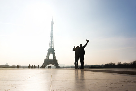 Couple at Eiffel Tower. Travelers and tourists exploring the world and the city of Paris. Romantic lovers on honeymoon or friends having fun. Silhouette people sightseeing. Wanderlust and travel.の写真素材