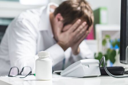 Stressed doctor cover face under pressure. Sad nurse, tired physician or upset doc. Medic crying in hospital office. Malpractice, treatment error and mistake or negligence. Workplace bullying.の写真素材