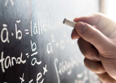 Teacher writing to blackboard with chalk. Student and chalkboard. Professor in school, college or university classroom. Science and education concept. Math formula or equation. Lecture or lesson.の写真素材