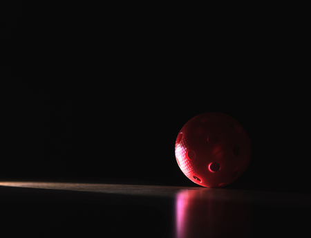 Black and dark floorball background with negative copy space. Red ball in spotlight in shadow.の写真素材