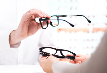Optician giving new glasses to customer for testing and trying. Eye doctor showing patient lenses in spectacles store. Professional optometrist in white coat with client.の写真素材