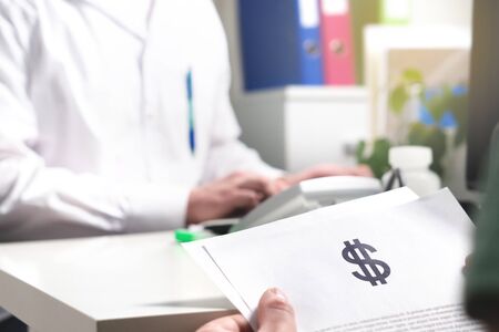 Medical and health care prices concept. Patient holding paper document, insurance, bill or invoice with dollar sign in doctor office in hospital or emergency room. High costs or expenses in healthcareの写真素材