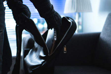 Home burglary and robbery. Burglar and thief stealing and putting stolen laptop in bag late at night. Theft, house security and insurance concept. Criminal man with black leather gloves.の写真素材