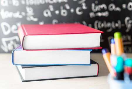 Stack and pile of books on table in front of a blackboard in school classroom. Education, studying,...