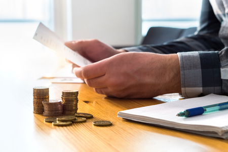 Man reading bank statement, check reminder, tax refund document, phone bill, or financial letter. Home or health insurance price and cost concept. Person holding paper invoice in hand.の写真素材