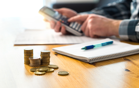 Man planning family finance and using calculator. Counting savings, budget, taxes, expenses and living cost. Calculating money. Accountant working on table and desk.の写真素材