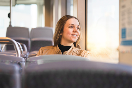Happy lady looking out the window in bus, train, tram or subway. Smiling woman riding public...