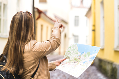 Tourist with map in the city. Woman pointing at right direction with finger. Back view of happy...