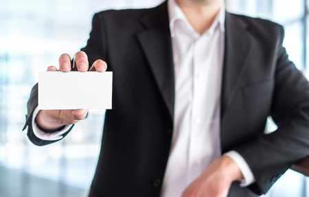 Casual business man holding empty white business card in modern office building. Free blank copy space.の写真素材