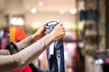Woman holding jeans and shopping in fashion clothing store. Person choosing trendy skinny jeans in clothes shop.の写真素材