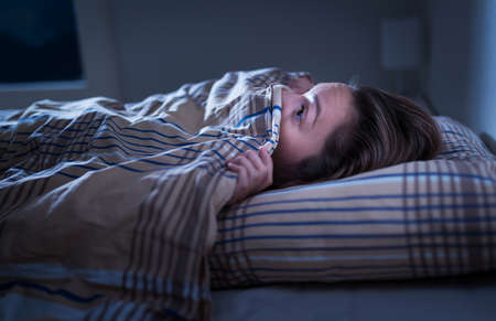Scared woman hiding under blanket. Afraid of the dark. Unable to sleep after nightmare or bad dream....