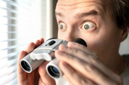 Surprised man with binoculars. Curious guy with big eyes. Nosy neighbour stalking or snooping secrets, gossip and rumour. Silly funny face. Shocked about unbelievable news. Stalker peeping people.の写真素材