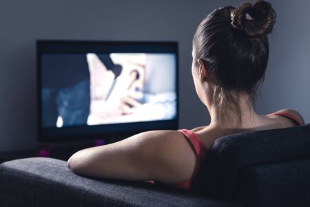 Young woman watching horror movie on online stream service. Girl streaming scary film or series at night. Fear and terror during thriller on tv. Video on demand (VOD) technology in television.の写真素材