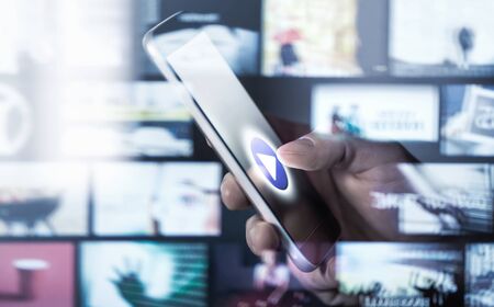 Watching movies and series with smartphone. On demand (VOD) service. Future multimedia technology in mobile phone. Man pressing play button. Entertainment of tv network. Many online video thumbnails.の写真素材