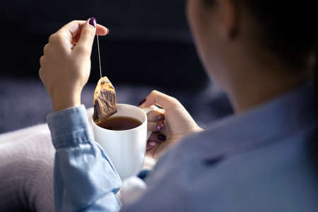 Woman holding tea bag in cup to make a healthy hot beverage in winter. Something warm for the cold season. Organic herbal teabag. Peaceful mood on weekend morning. Sick person with fever or flu.の写真素材