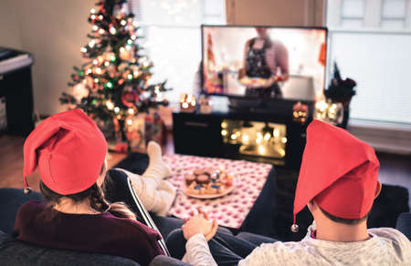 Couple watching tv on Christmas. Happy family holiday at home. Man and woman on couch relaxing with tree, decorations, lights, candles and television. Modern city celebrations. Merry Xmas!の写真素材