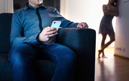 Jealous woman and cheating man with a phone. Infidelity, jealousy and betrayal. Cheater husband texting with mistress and secret lover. Suspicious wife peeking and spying. Unfaithful sneaky boyfriend.の写真素材