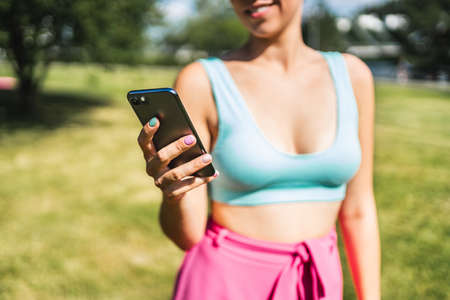 Girl using phone and texting in summer in outdoor park. Woman looking sms message with smartphone. Fit person with cellphone outside in garden wearing bikini. Trendy lifestyle and mobile technology.の写真素材