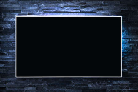 Tv screen on wall at night in dark with led light. Television and flat smart monitor display on blue brick background. Modern futuristic loft living room or lounge. Empty black flatscreen.の写真素材