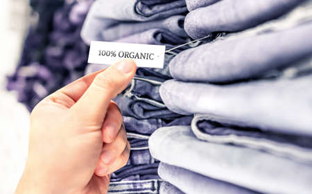 Organic jeans, ethical denim pants. Stack of clothes in store shelf. Label and tag. Sustainable retail fashion and quality product made from natural fabric and textile. Customer buying trousers.の写真素材