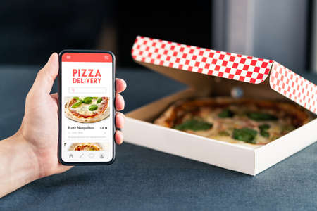 Pizza delivery and food app in phone. Online order restaurant take away. Lunch menu in cellphone screen with takeout box. Hungry customer using website with review and rating. Takeaway service.の写真素材