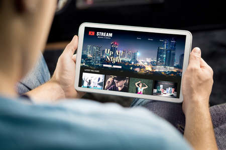 Movie and series stream VOD service in tablet. Watching on demand tv show or film online. Man choosing video entertainment from subscription media catalogue. Streaming website library mockup.の写真素材