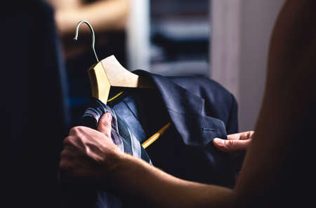 Man getting ready and dressing up in a suit. Luxury jacket and tie in hanger. Trying on outfit before date or wedding. Fitting room in mall store, closet or tailor shop. Formal businessman fashion.の写真素材