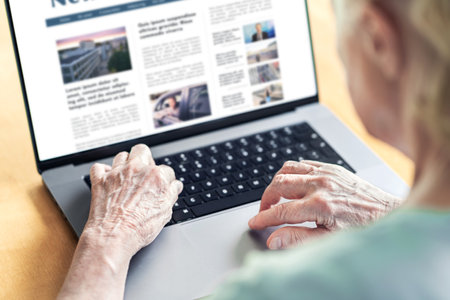 News website in laptop of an old woman. Elder senior and grandma reading digital newspaper with computer. Online magazine or web article in screen. Daily information publication site by the press.の写真素材