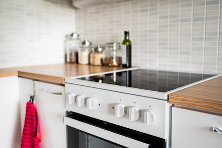 Kitchen with cooking stove, oven and table. Cabinet design in small home. Electric ceramic induction...