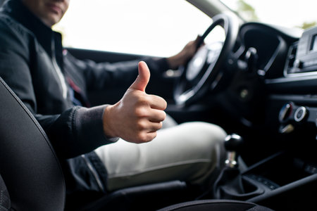 Happy driver in car, thumbs up. Man driving. Smiling positive new vehicle buyer and owner. Good customer service in taxi, dealership, insurance, inspection or maintenance business. Success in repair.の写真素材