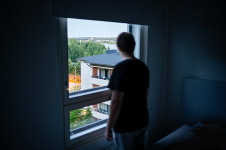 Man and window in dark room. Spying neighbor or snooping. Loneliness, shame or melancholy. Depressed, sad, moody or paranoid. Mental health, depression. Creepy person stalking. Stalker in home bedroomの写真素材