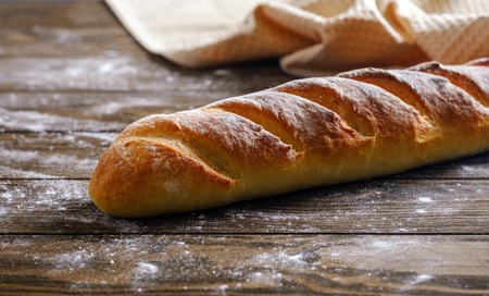 Fresh French loaf with a ruddy crust on a wooden tableの写真素材